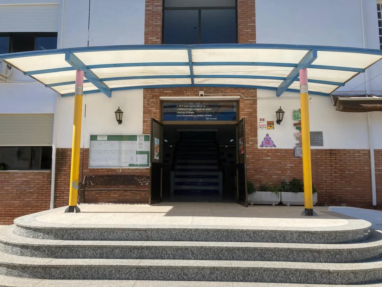 La entrada del colegio: una marquesina azul sostenida por dos columnas amarillas con forma de lápiz.